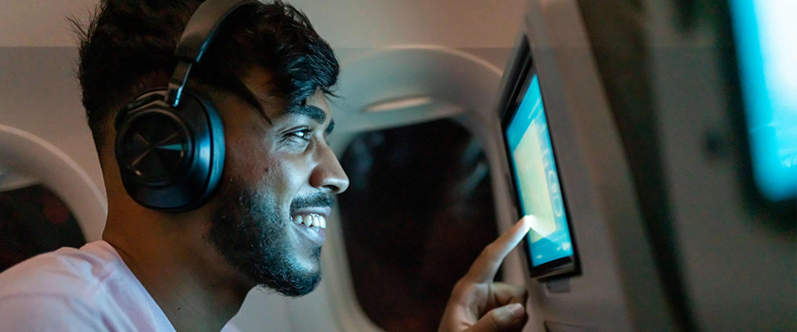 A passenger on a flight smiles as he uses a screen on a seat back