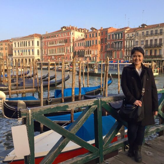 A woman standing near a water canal lined with boats