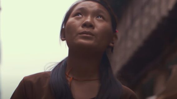 A woman looks up at the sky in a city street.