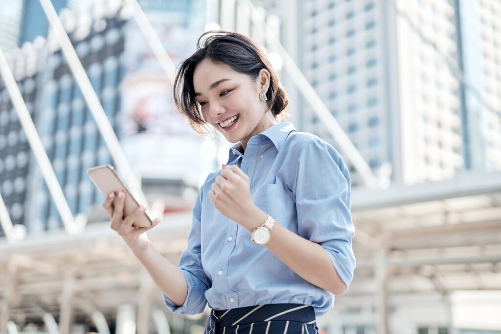 Asian woman using a smartphone while walking through a bustling city street.
