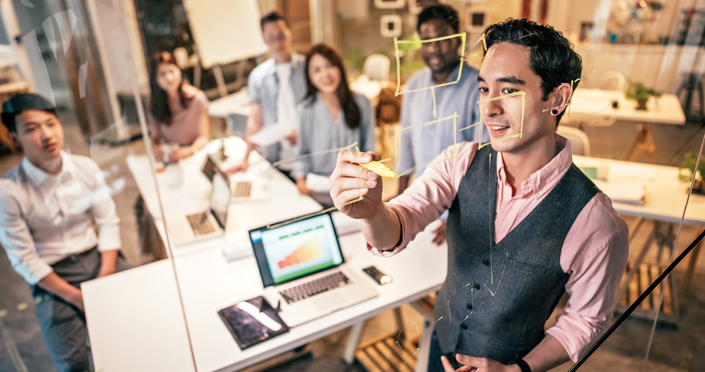 Man writing on glass in front of people