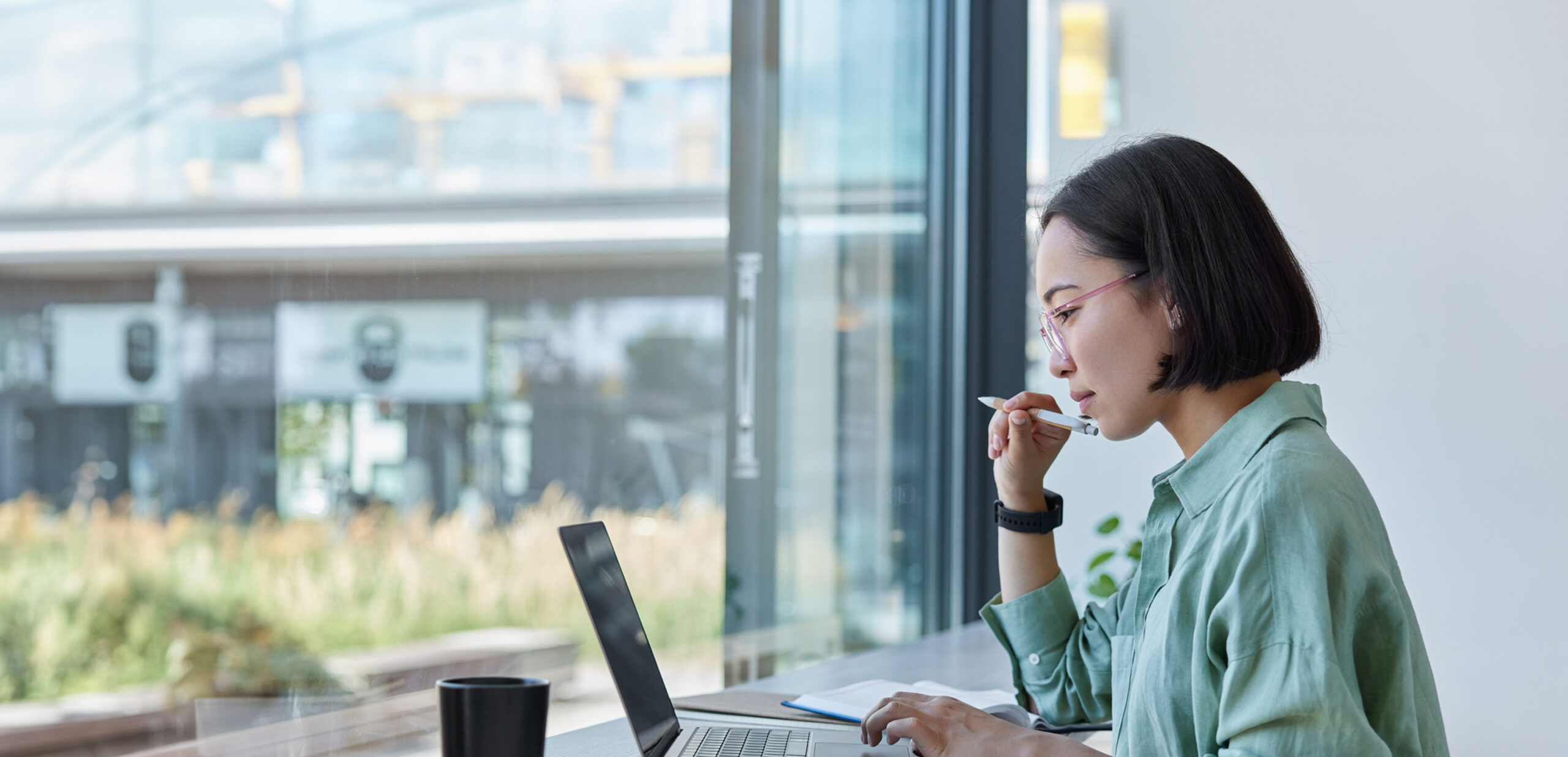 A woman reporter types on her laptop by a bright window.