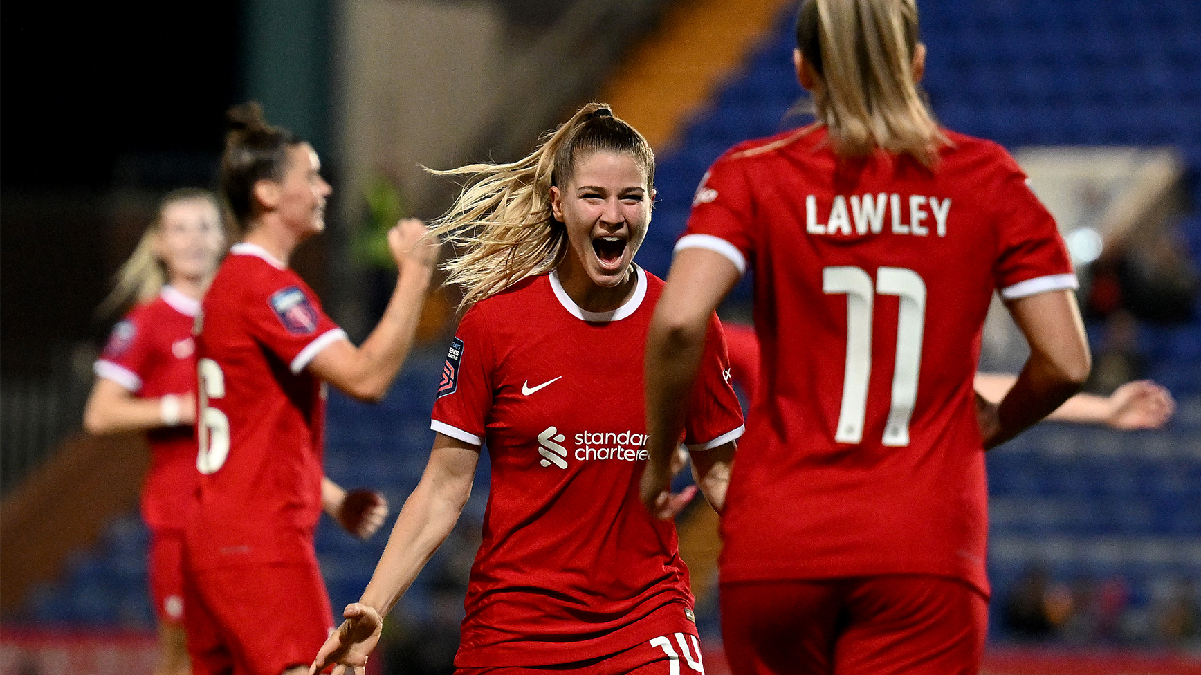 LFC players celebrate on the pitch, wearing the iconic red shirts with the Standard Chartered logo.